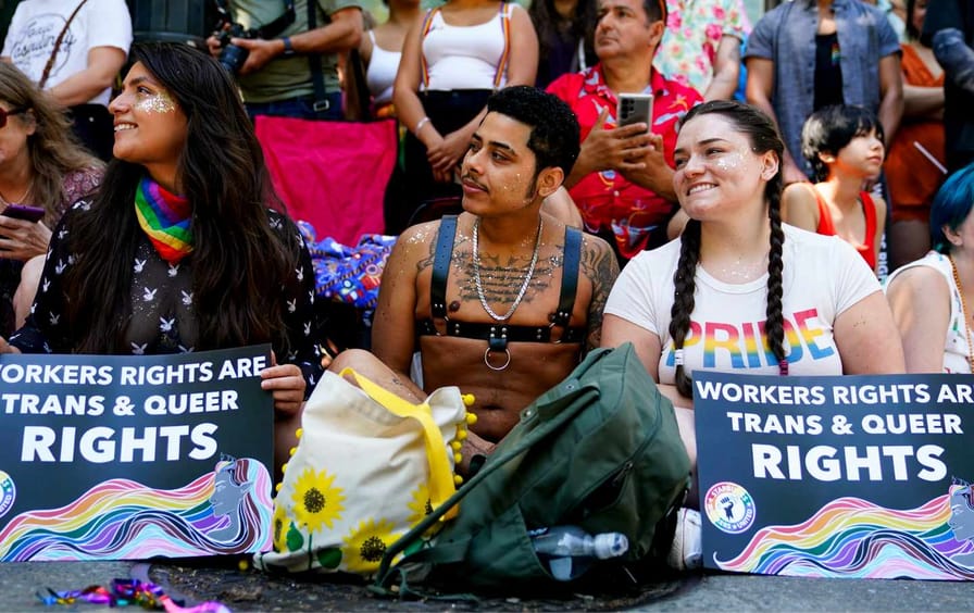 Jessica Garcia, Erik Garcia and Meara White hold signs in support of Starbucks workers as they watch marchers in the annual Seattle Pride Parade on June 25, 2023.