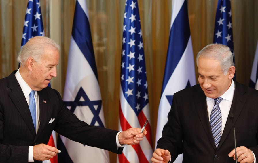 Biden hands Netanyahu a pen. US and Israeli flags seen in background