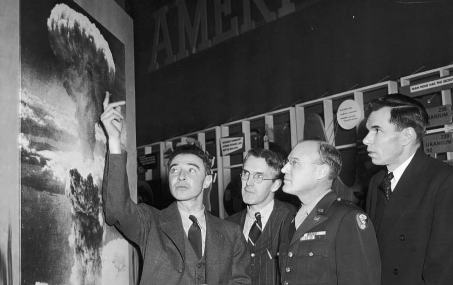 J. Robert Oppenheimer pointing to an image of the atomic bomb explosion