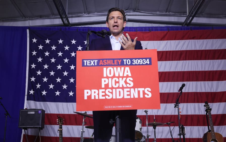 Ron DeSantis in front of a large American flag and a sign reading “Iowa Picks Presidents.”