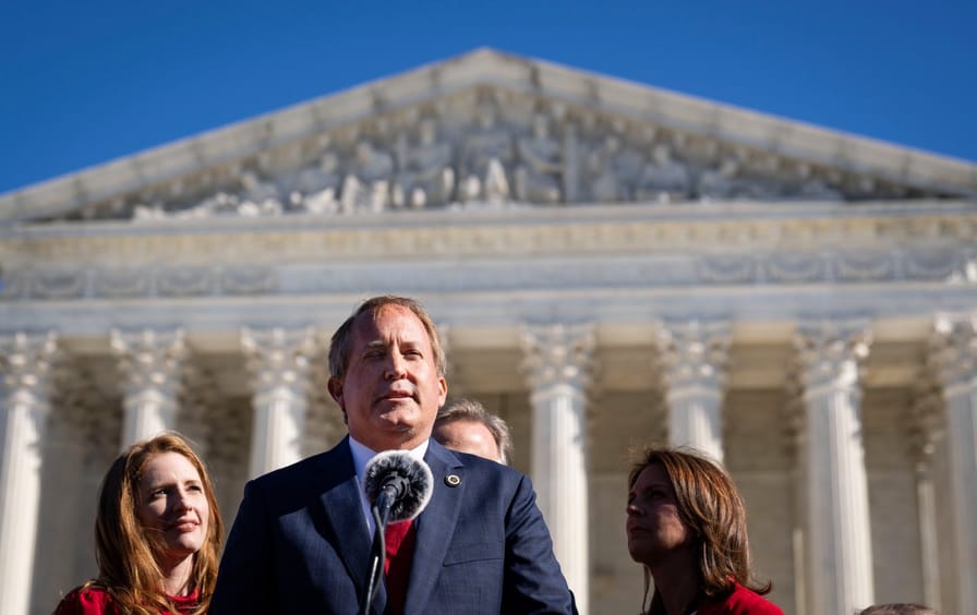 A closely framed photo of Ken Paxton at a microphone in front of the Supreme Court Building.