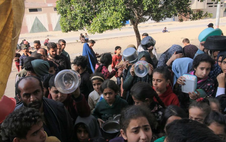 A group of Palestinians, mostly children, hold out empty containers for food.
