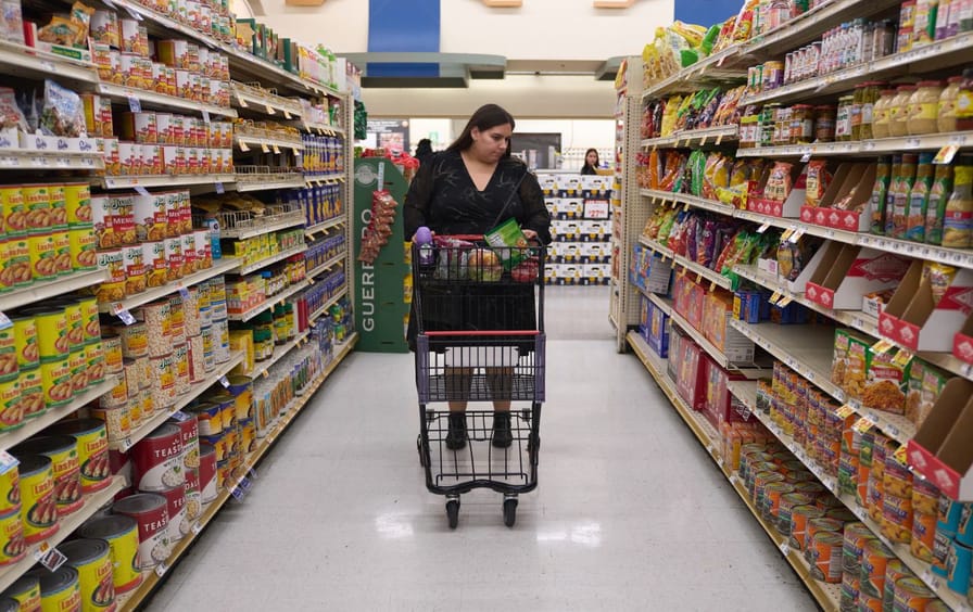 A woman standing with a shopping cart between tall aisles of a grocery store.