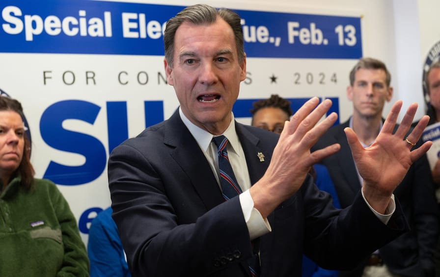 Tom Suozzi in a suit speaking in front of a sign announcing the special election in NY-03.