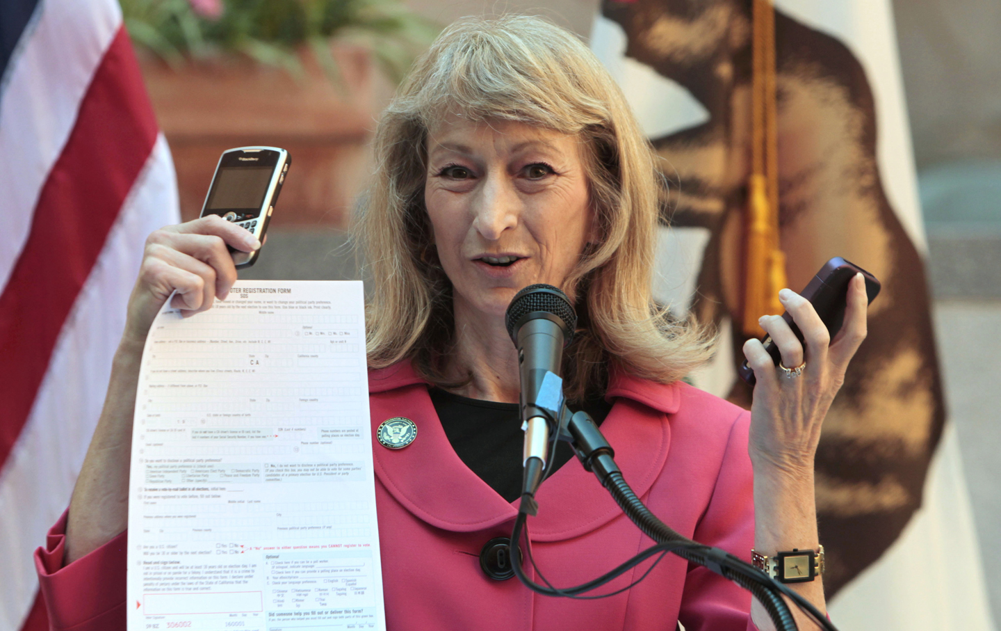 California Secretary of State Debra Bowen displays cellphones and a paper form following the signing of California's new online voter registration bill.