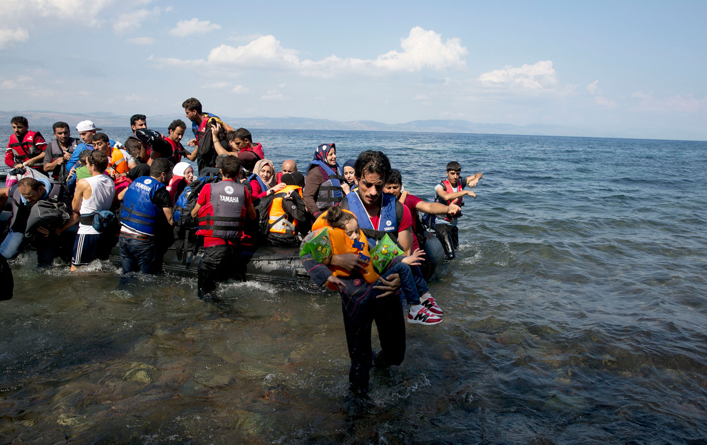 A man carries a child as migrants and refugees arrive on a dinghy after crossing from Turkey to Lesbos island, Greece.