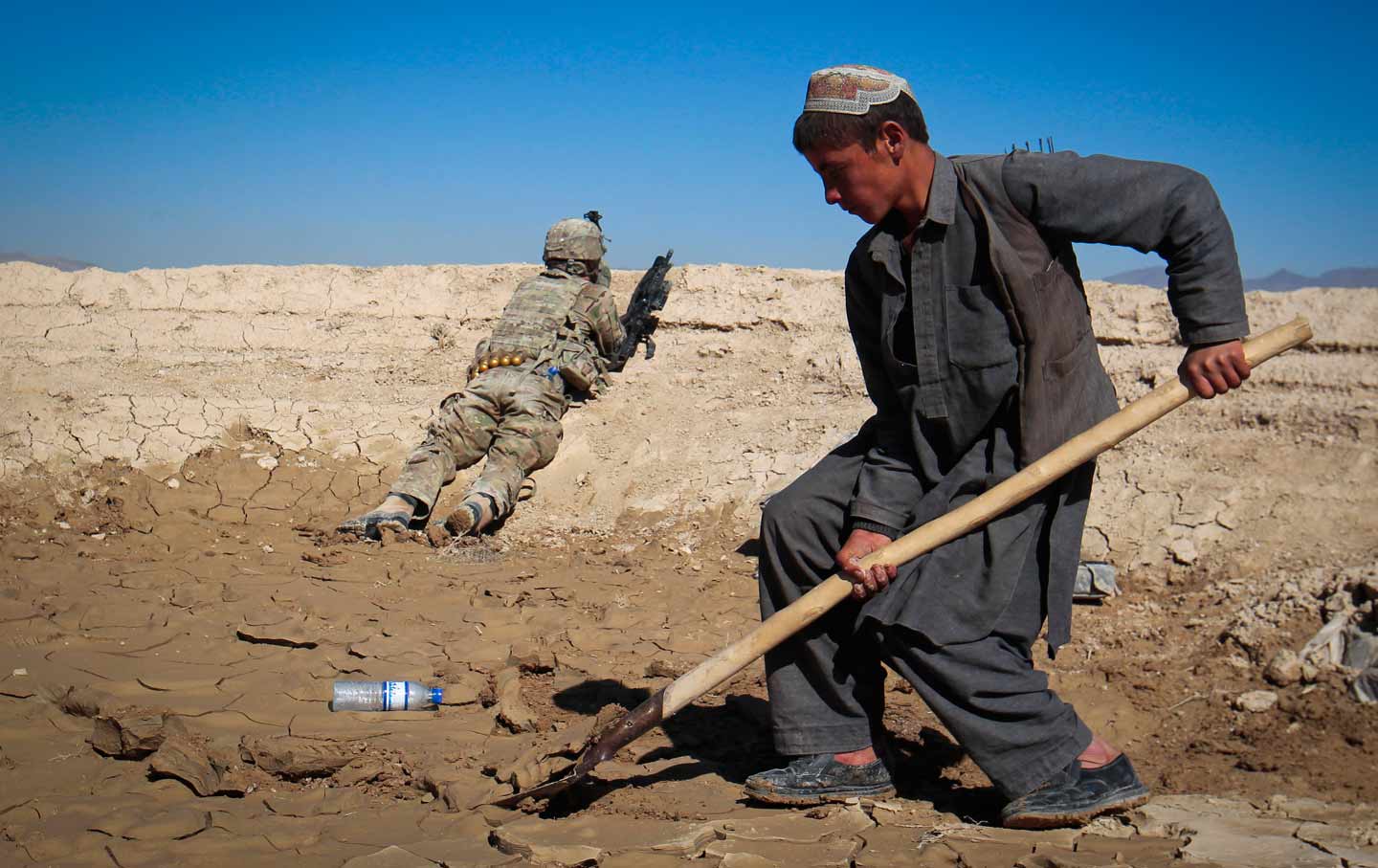 An Afghan boy works at a construction site behind a US Army soldier in Logar province, Afghanistan.