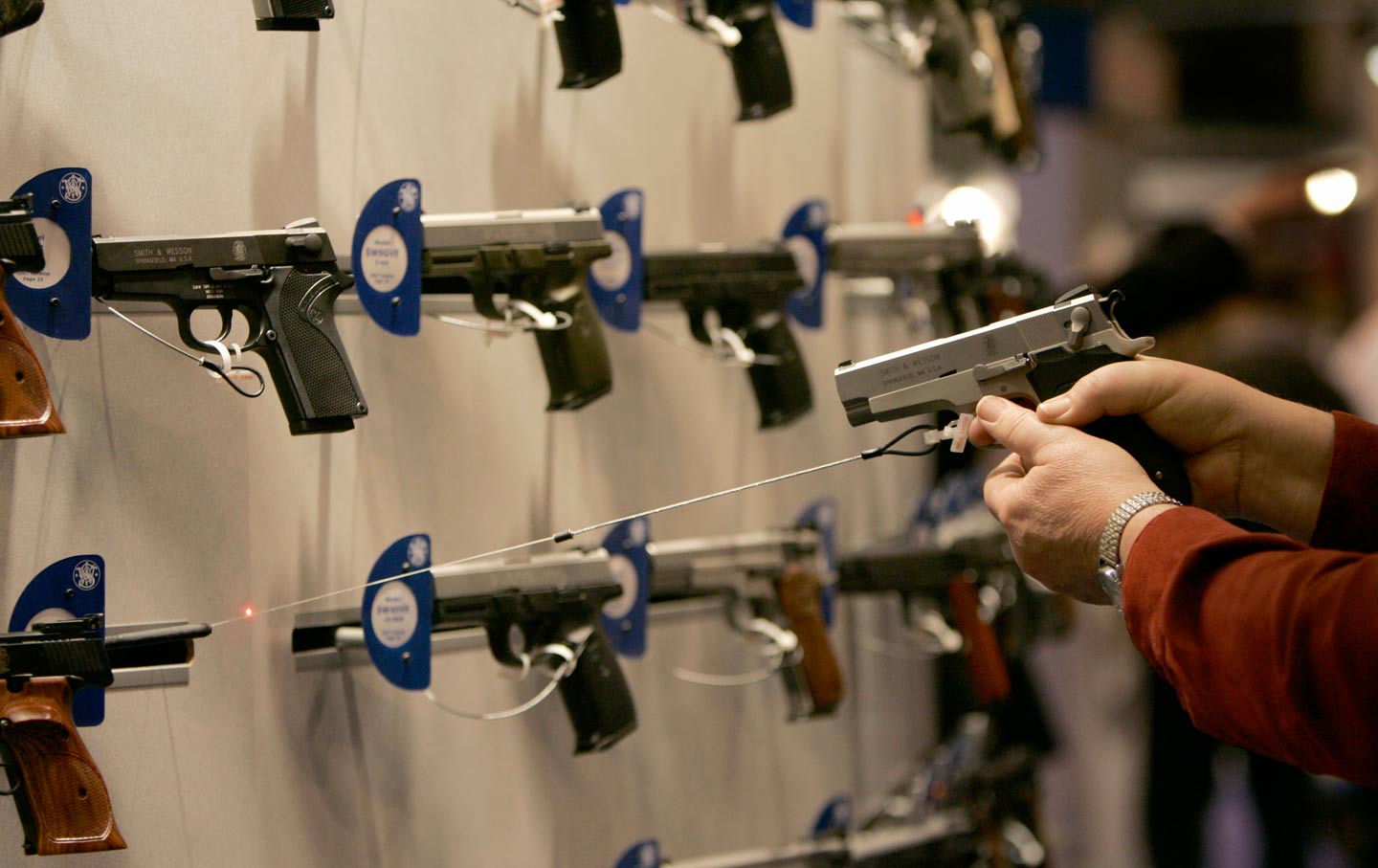 A woman points a handgun with a laser sight on a wall display of other guns during the National Rifle Association convention in St. Louis.