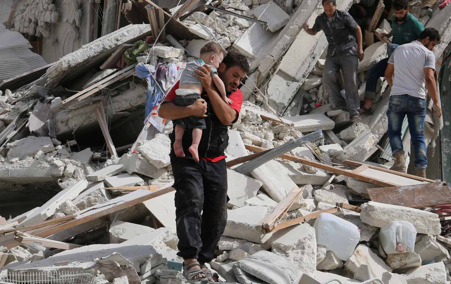 man carrying injured child from rubble