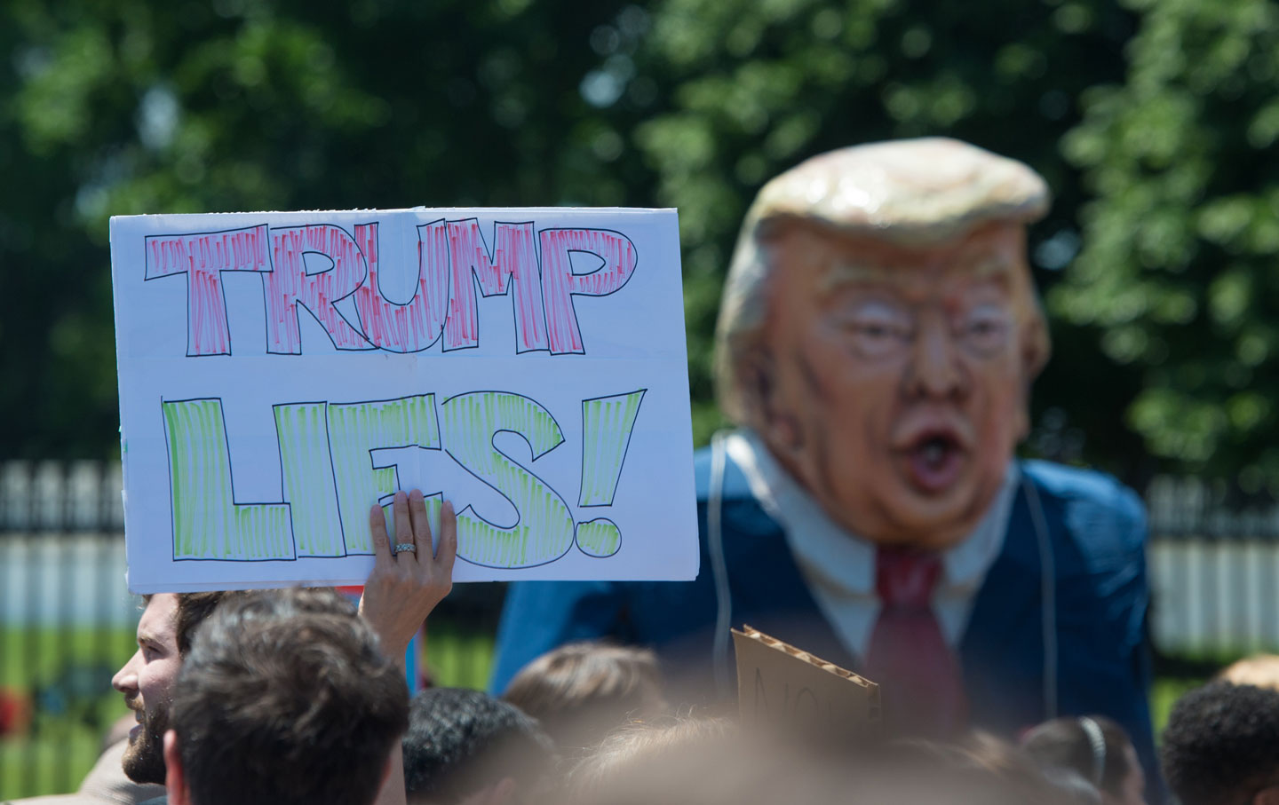 A protester holds up a sign while a person walks around in a caricature of Trump during a peaceful protest