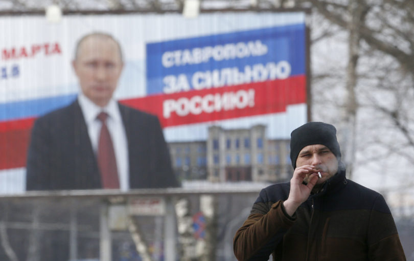 Man smokes in front of Putin billboard