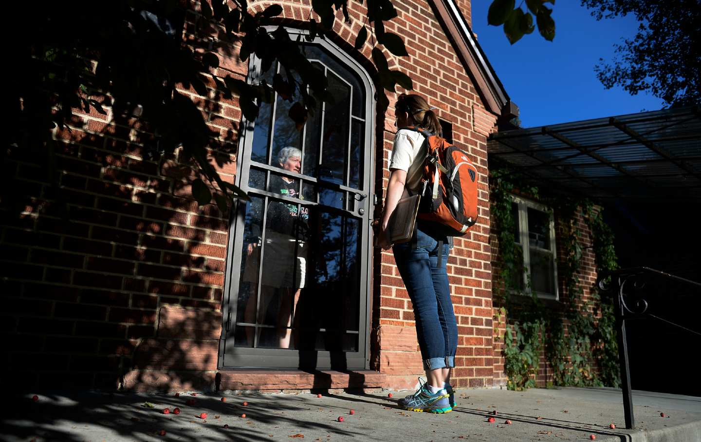 A volunteer speaks to an older voter through a glass door.