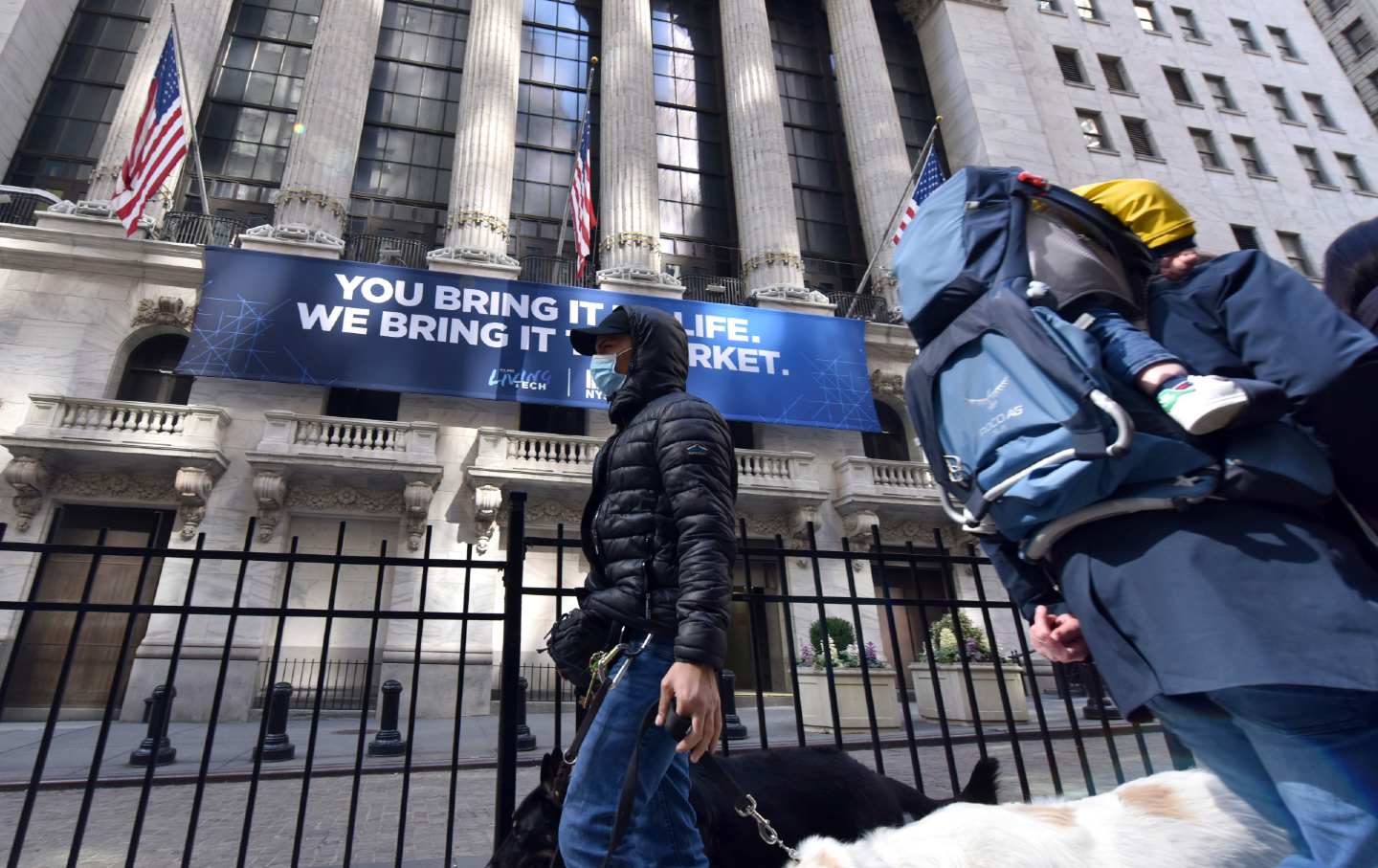 A man wearing a protective mask and passing in front of the New York Stock Exchange, walking his dog.