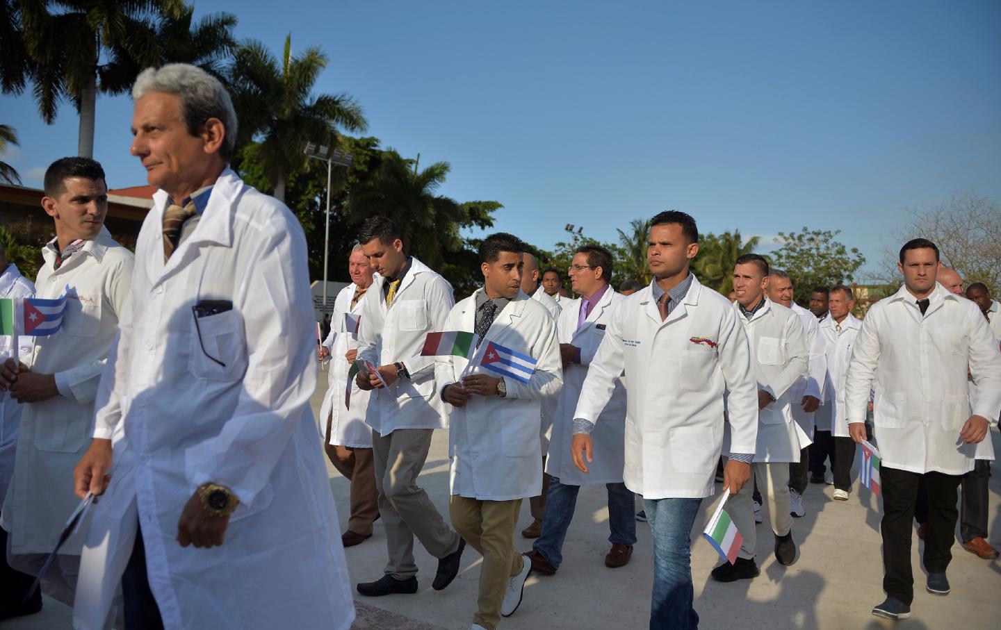 A group of doctors and nurses walk outside, holding small Cuban and Italian flags.
