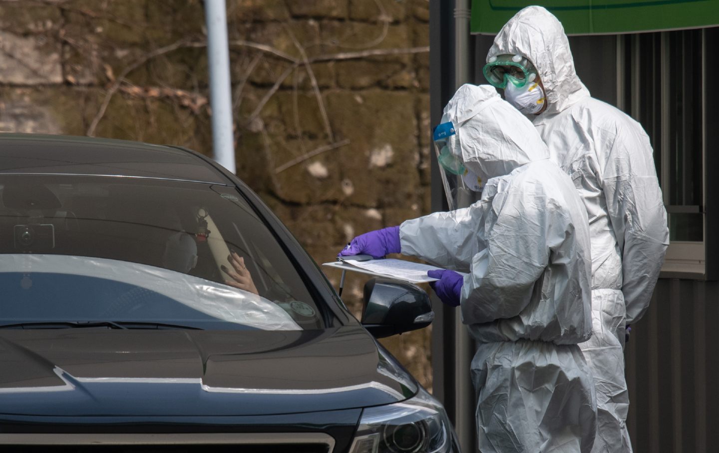 A driver in a car on the left talks to two health workers in protective suits.