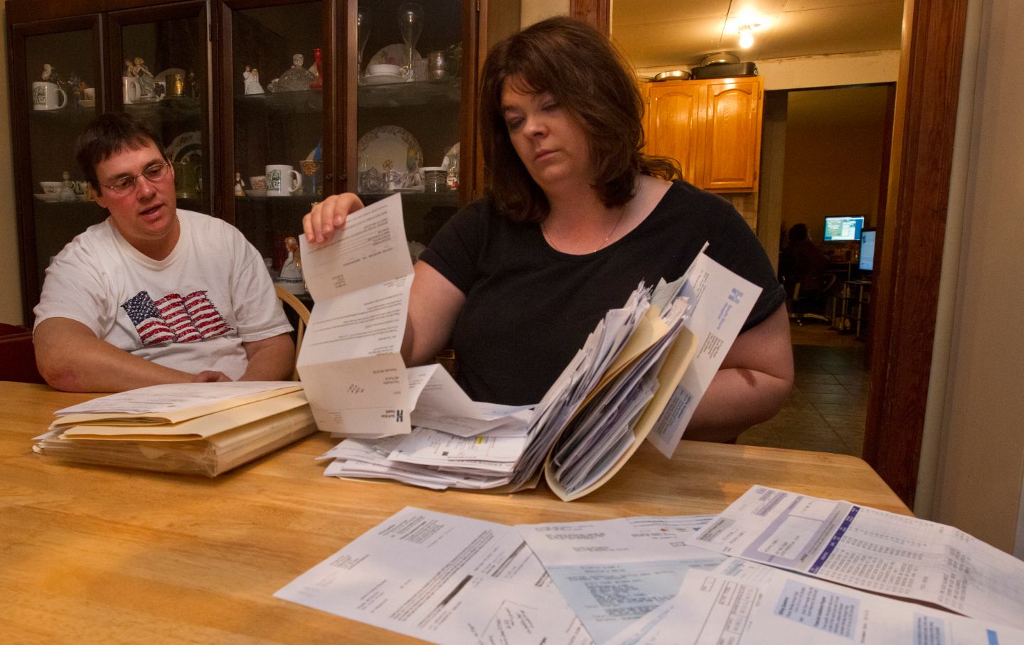 Glenn and Tracy McCarthy in their home with a pile of medical bills
