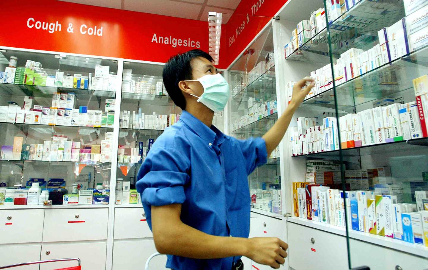 A pharmacist checks his stock while wearing a surgical mask.
