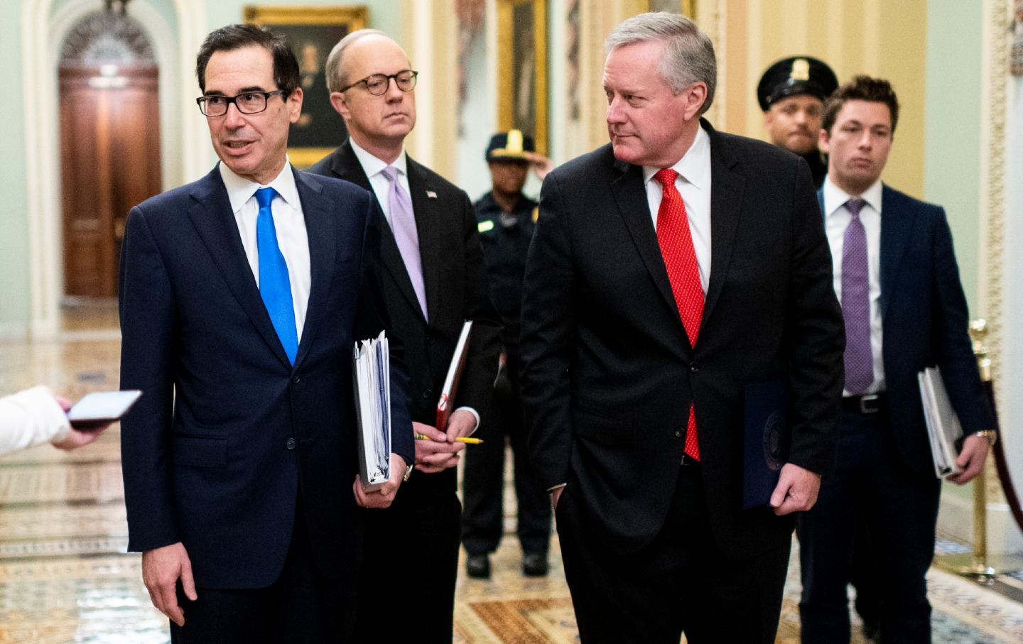 Three men in suits walk down a hallway of the Capitol building.