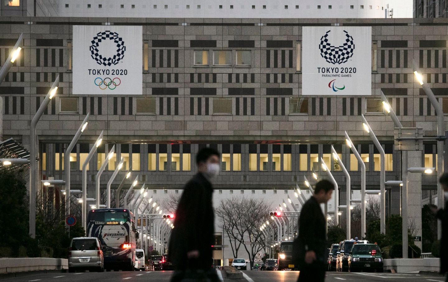 People walk across a pedestrian crossing near the Tokyo Metropolitan Government building adorned with signs promoting the 2020 Olympics.