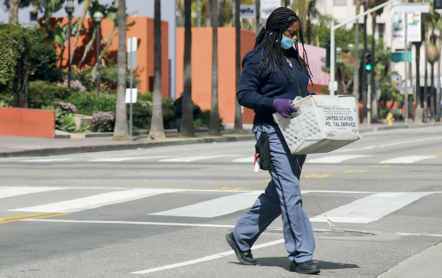 USPS worker with gloves and mask crosses street amid coronavirus outbreak in LA
