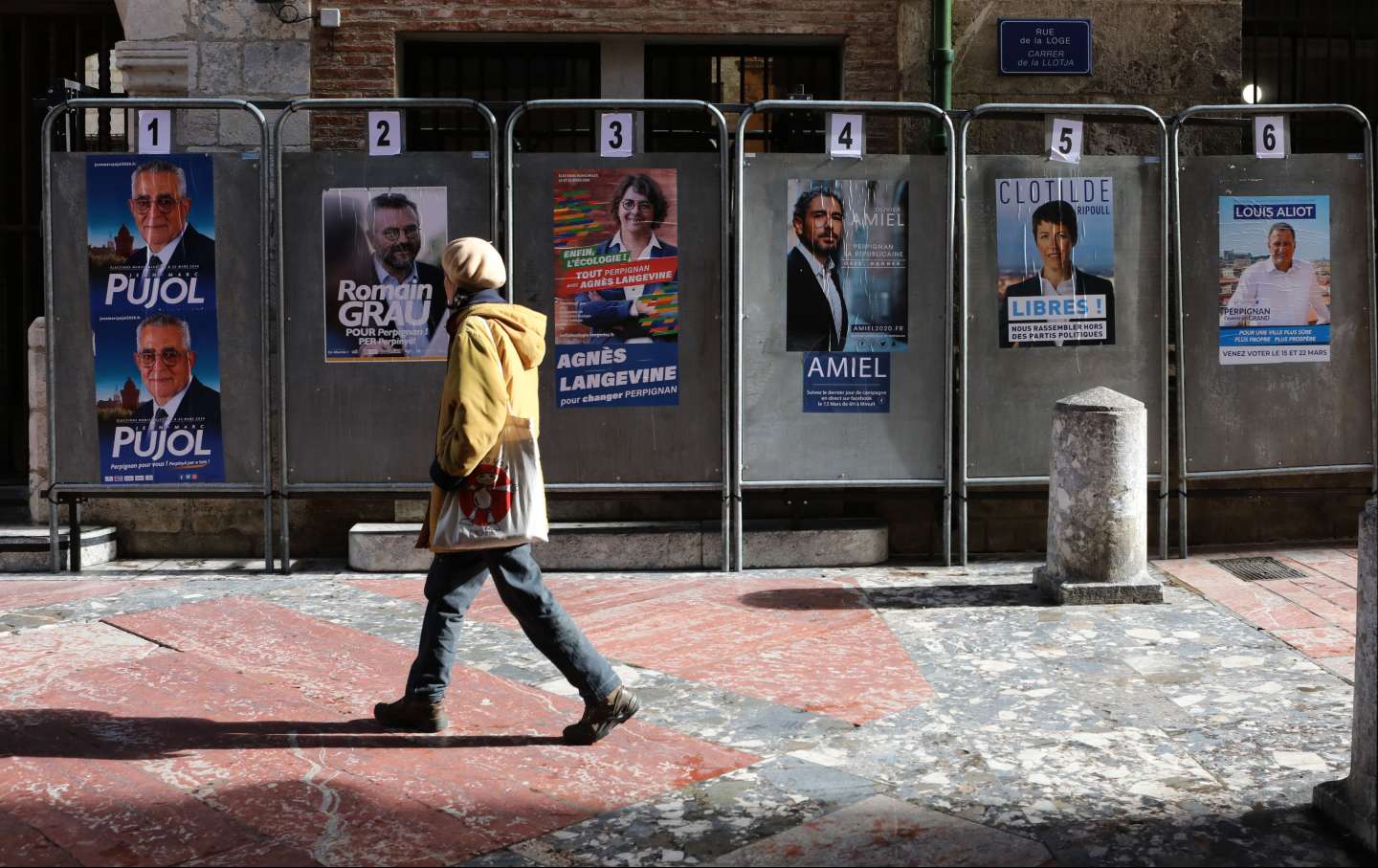 A woman walks by an posters in front of the city hall of Perpignan