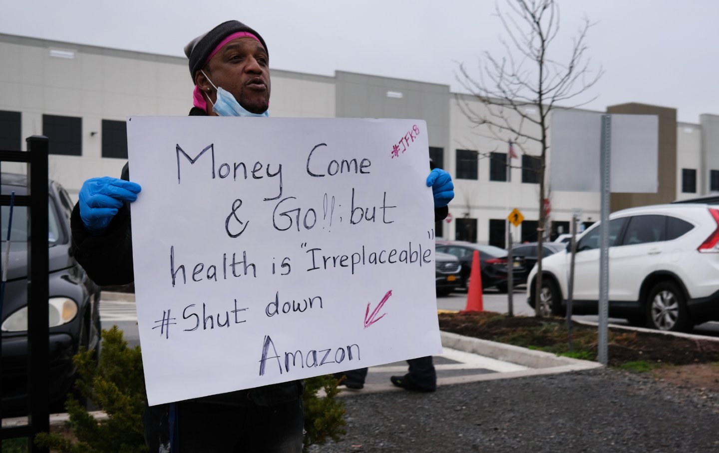 A worker stands outside an Amazon warehouse holding a sign that says