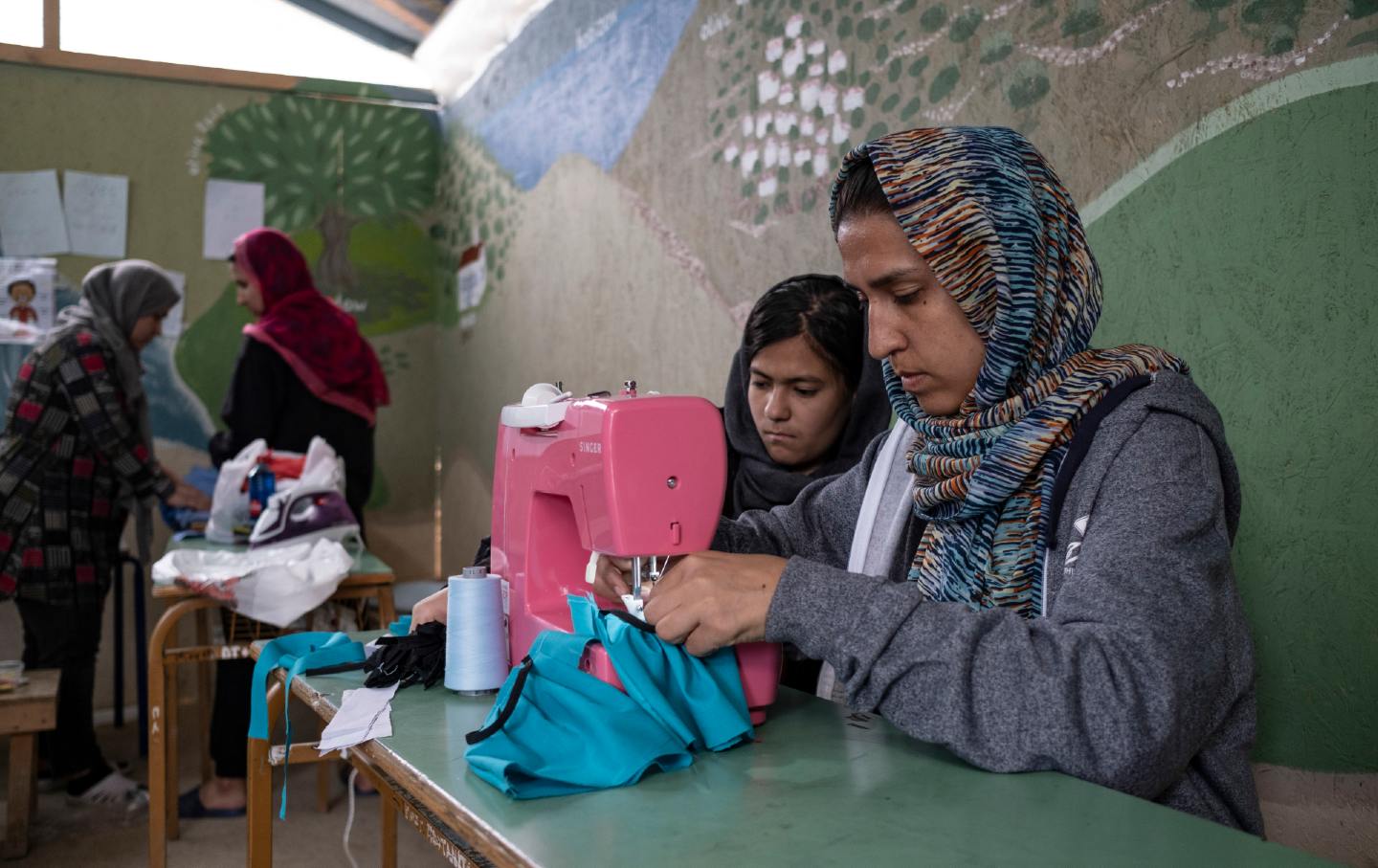 Two women focus on a sewing machine.