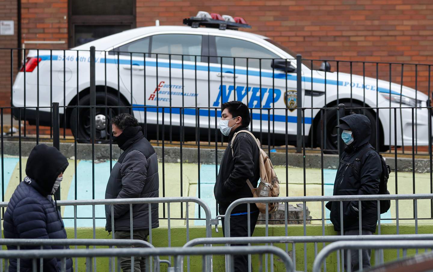 People wearing masks stand in line before entering a testing site at Elmhurst Hospital