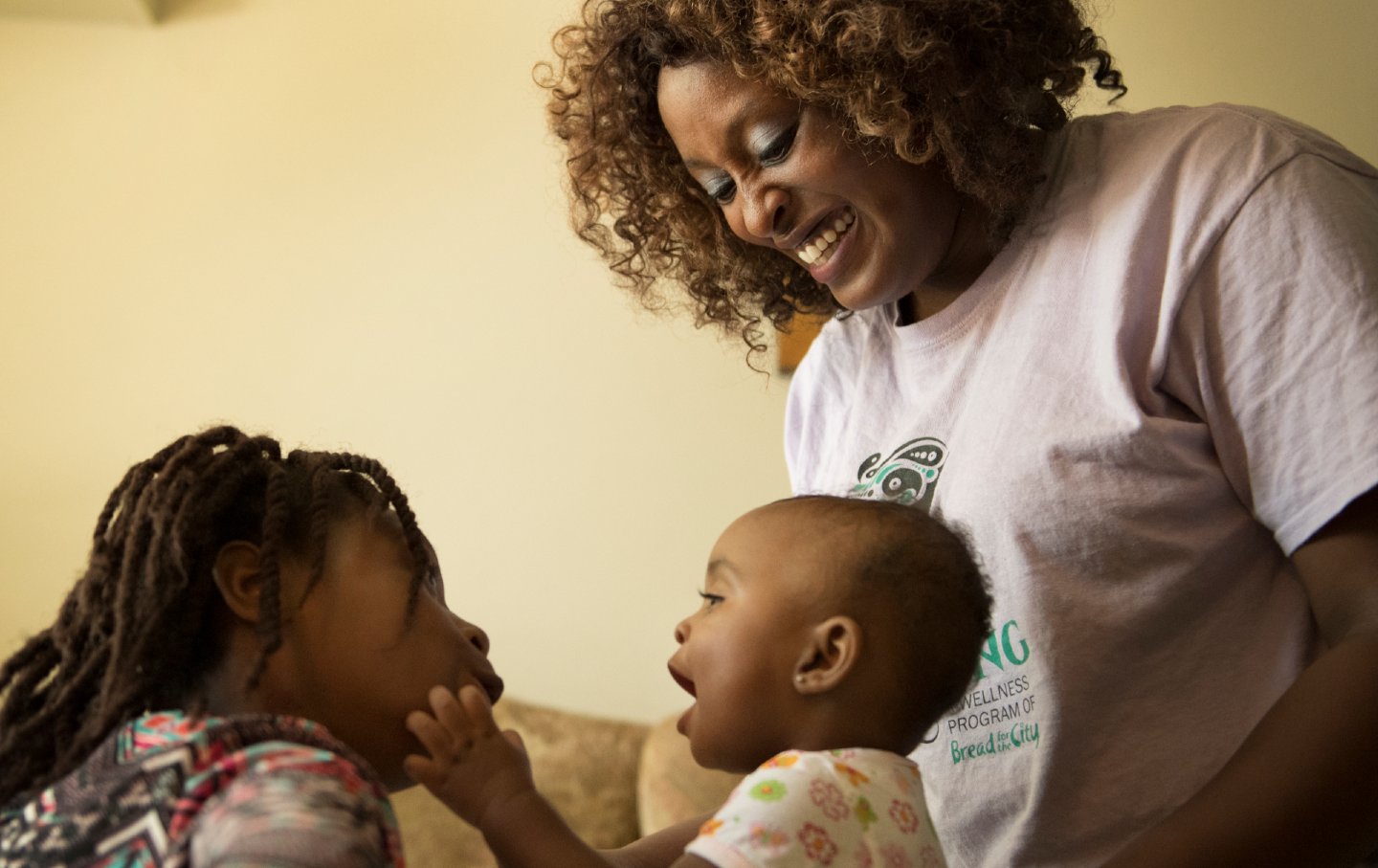 An African American woman plays with her two children, one is a baby and the other is 10 years old.