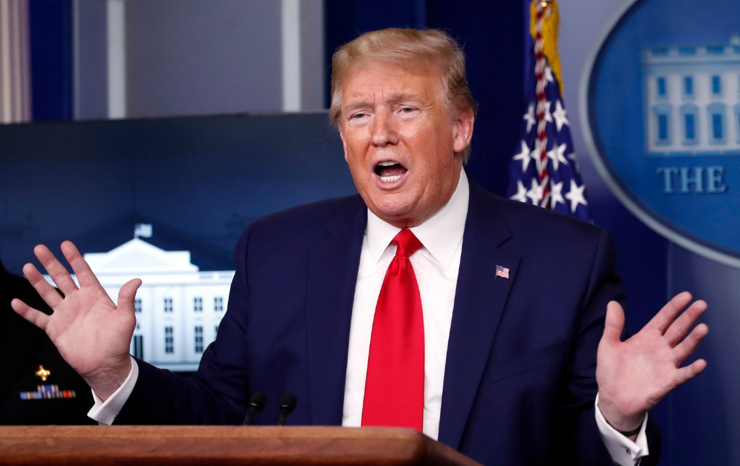 President Donald Trump speaks with his hands in the air while standing at a podium