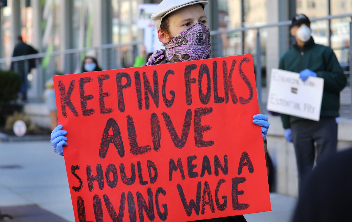 A man covering his mouth with a bandanna holds a sign that say 