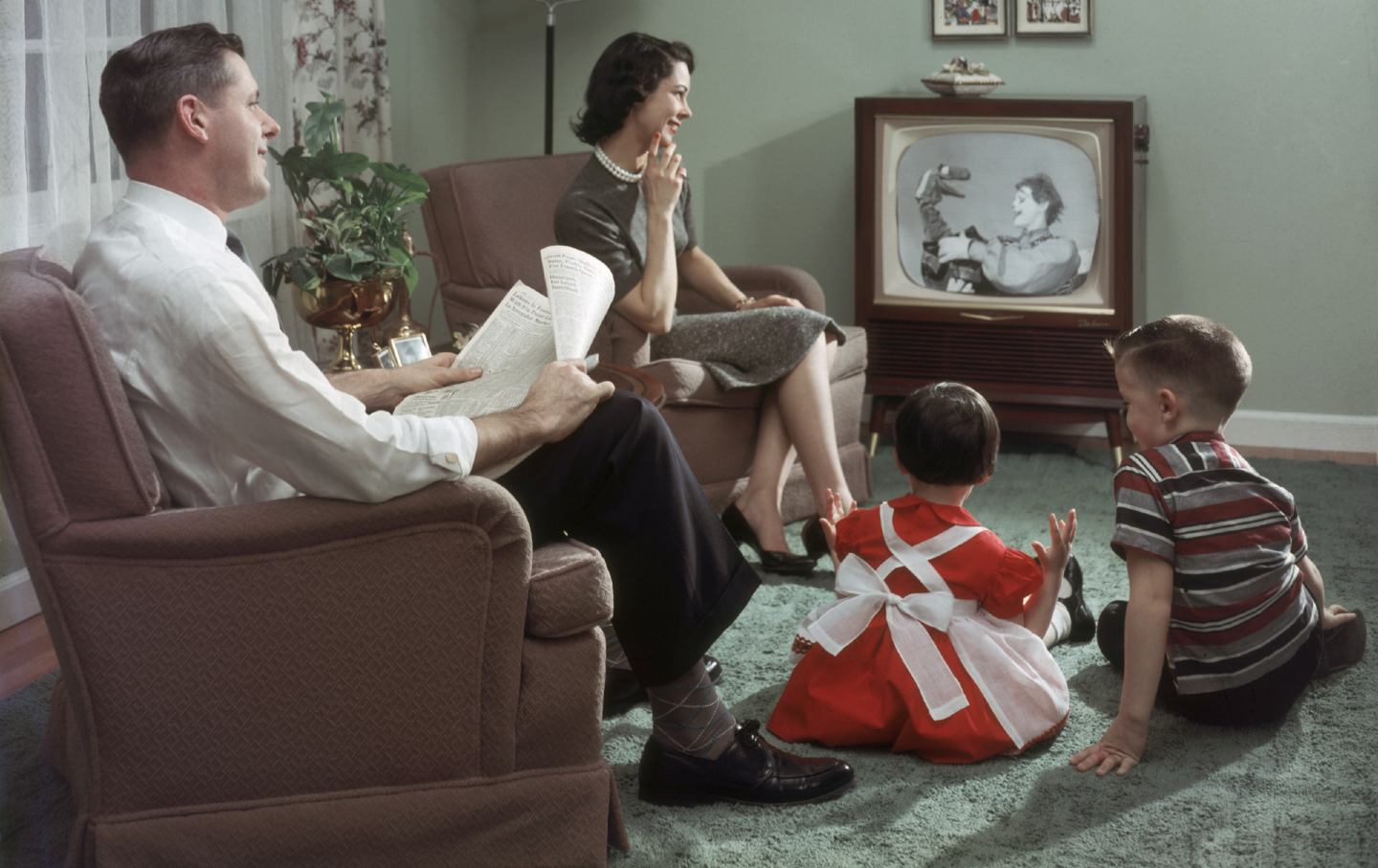 A man, a woman and two children sit around a television.