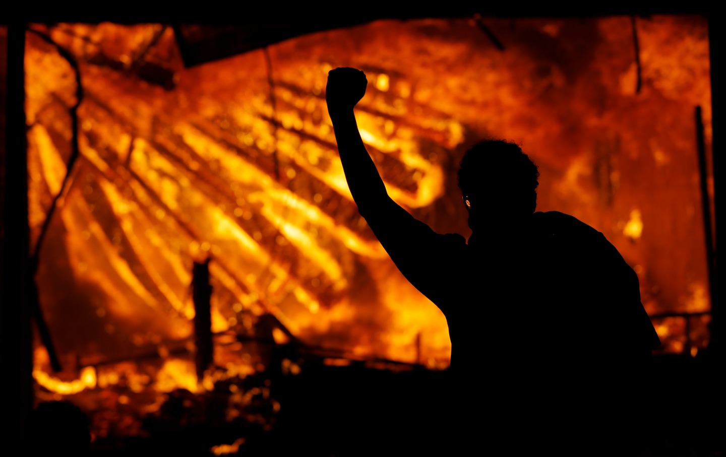 Person with arm raised in front of burning building