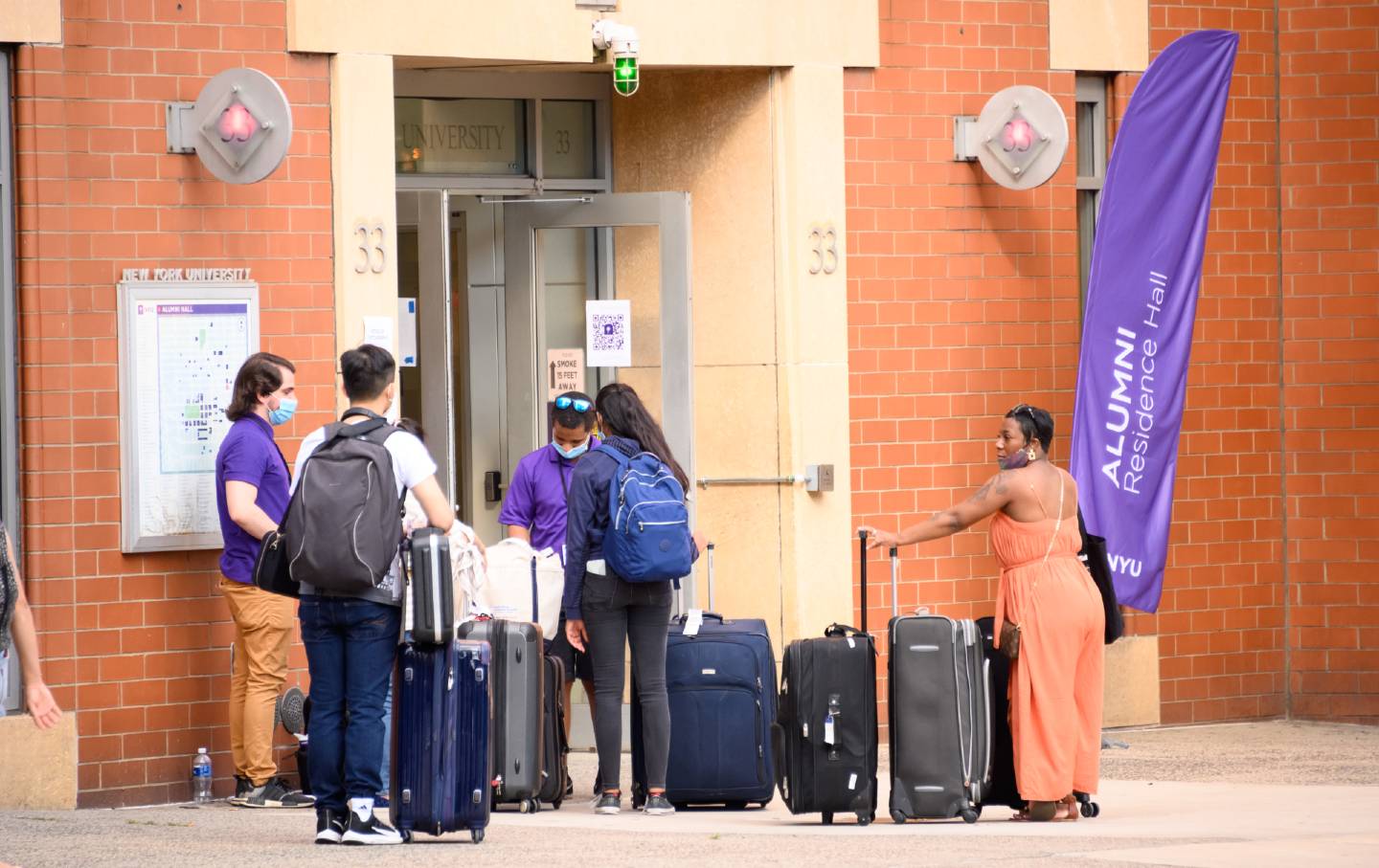 Two students and a parent, all wearing masks, check into NYU dorms.