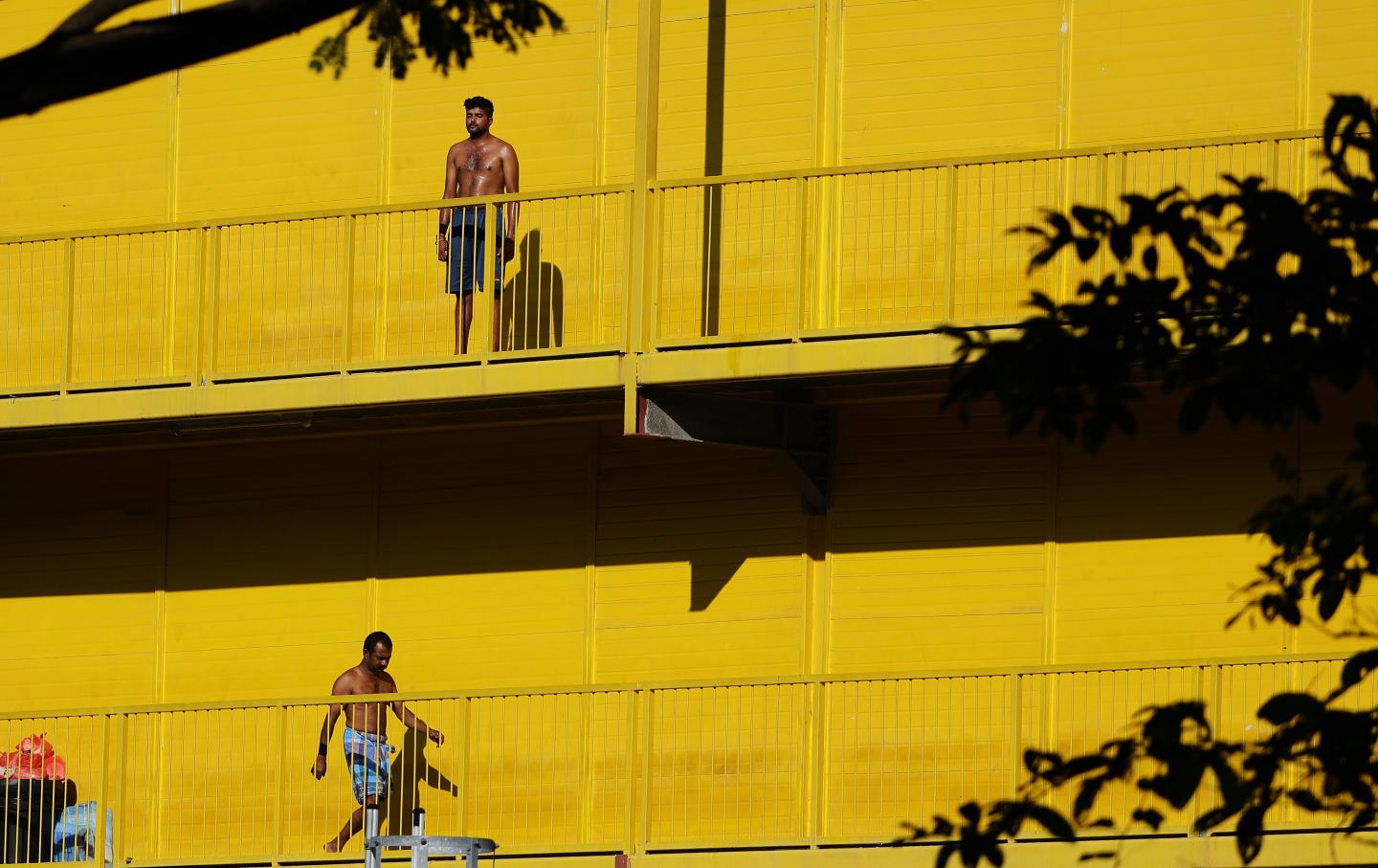 Men exercising without shirts against a yellow building in Singapore.