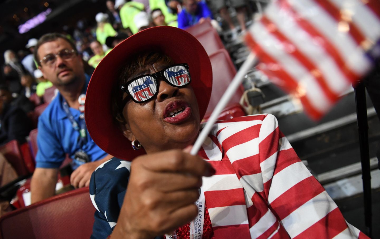 A delegate wearing Democratic Party sunglasses and an American flag suit waves an American flag.