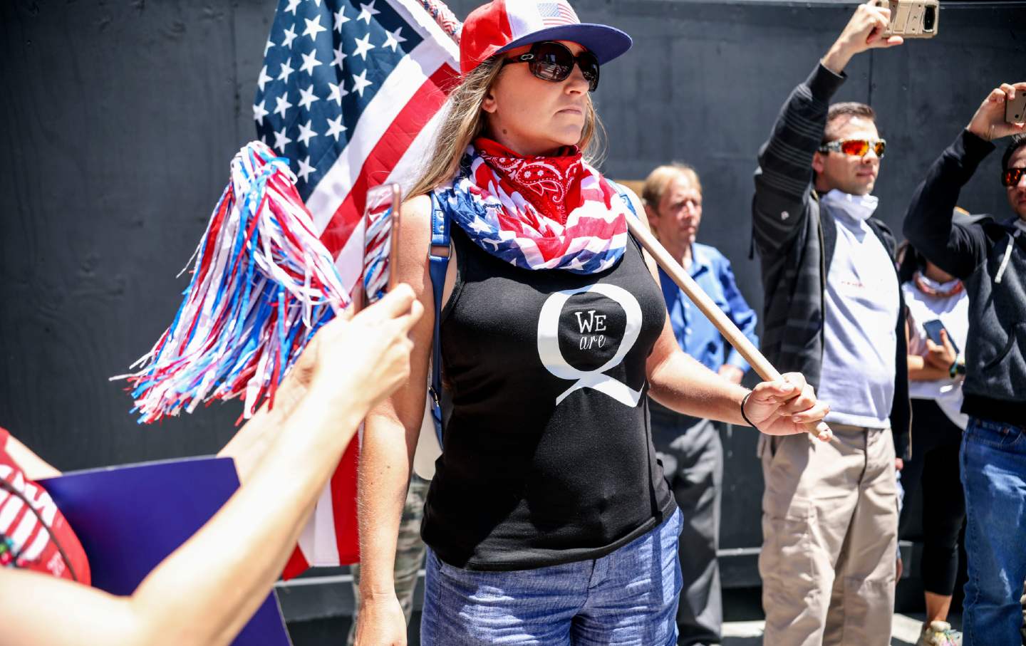 A woman in a shirt showing support for the QAnon conspiracy theory holds an American flag.