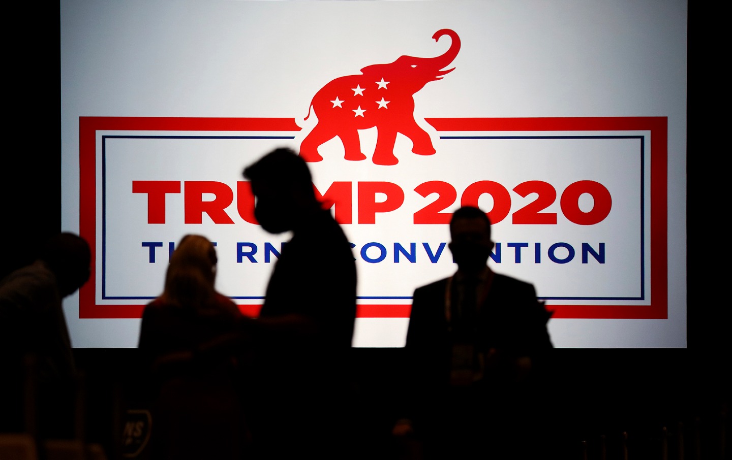 Silhouettes walk past a sign with the RNC logo and reads 