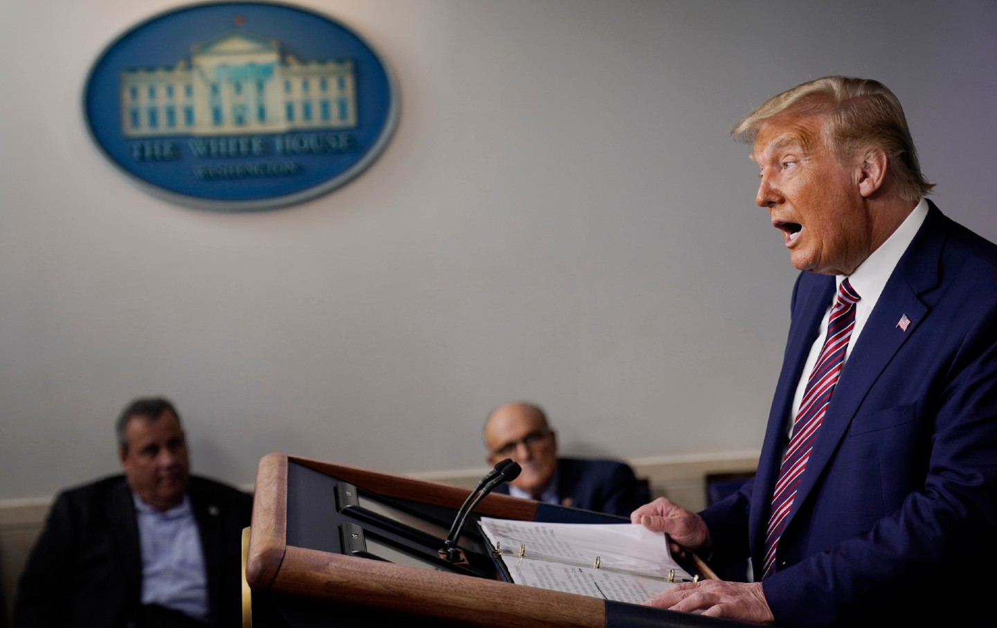 Donald Trump speaks on the right while Former New Jersey Gov. Chris Christie, and former New York Mayor Rudy Giuliani look on in the background.