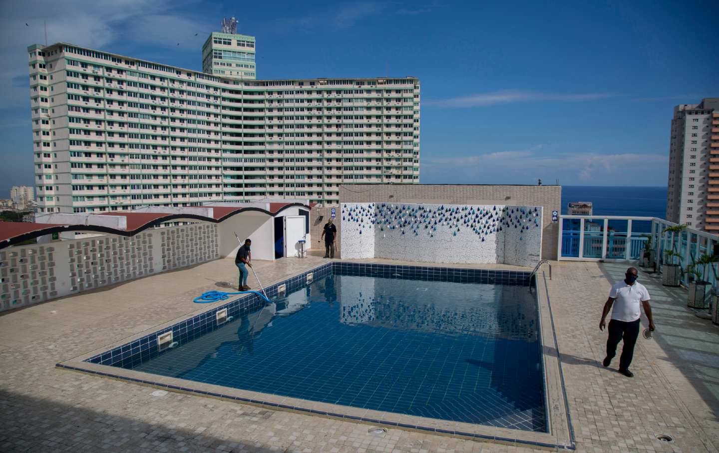 Workers clean a rooftop pool while a large building is seen in the background.