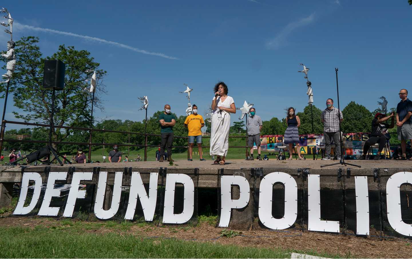 Woman speaks in front of sign saying 