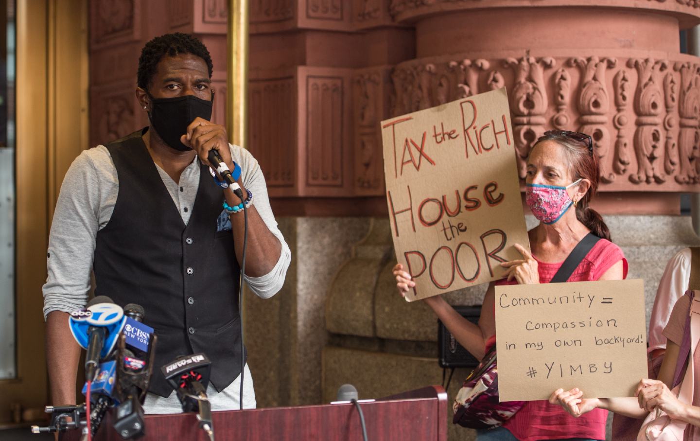 Jumaane Williams stands on the left while an unnamed protester stands on the right, holding a sign that reads 