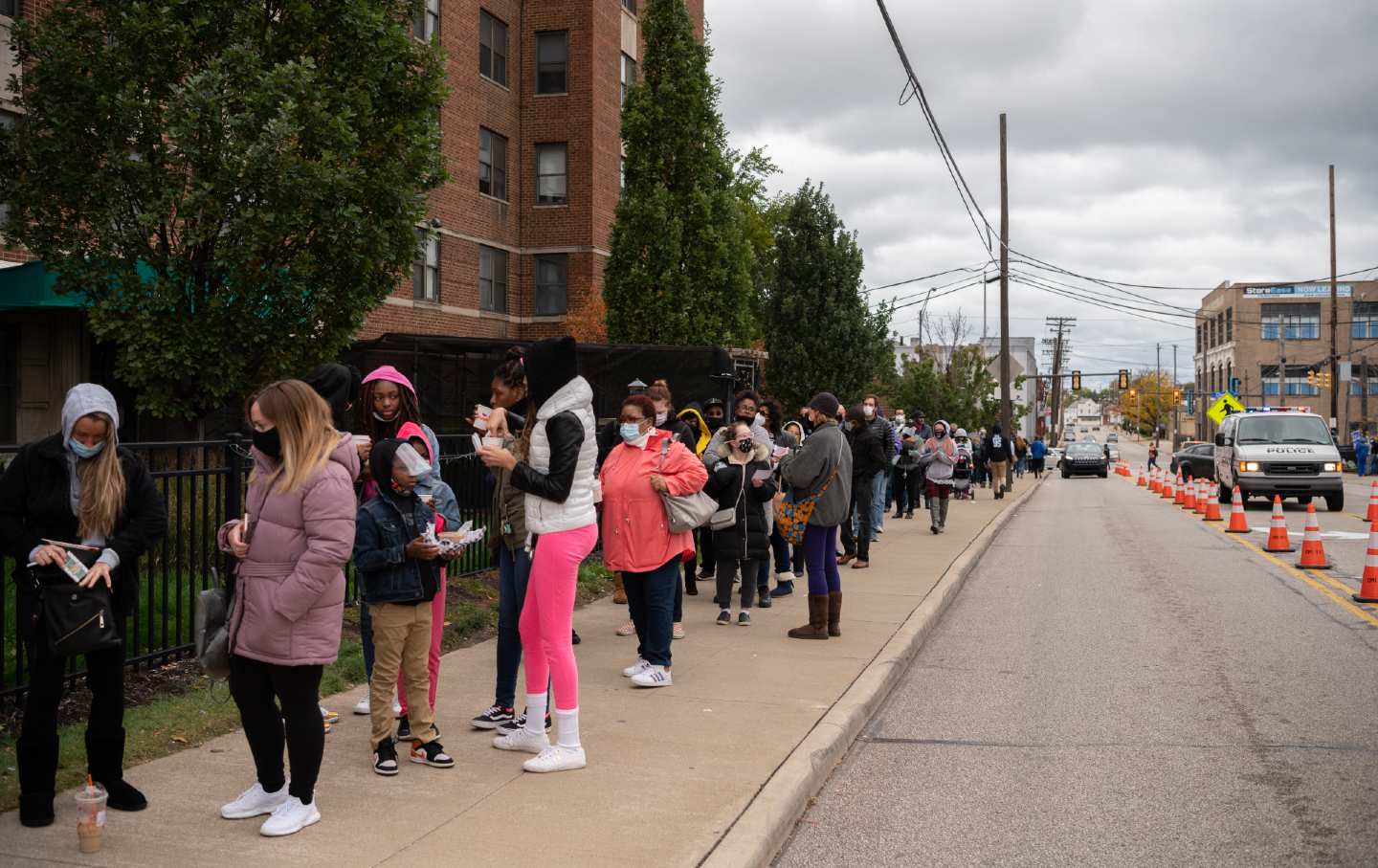 A line of voters stretches across a block on the left, while cars are seen driving down a road on the right.