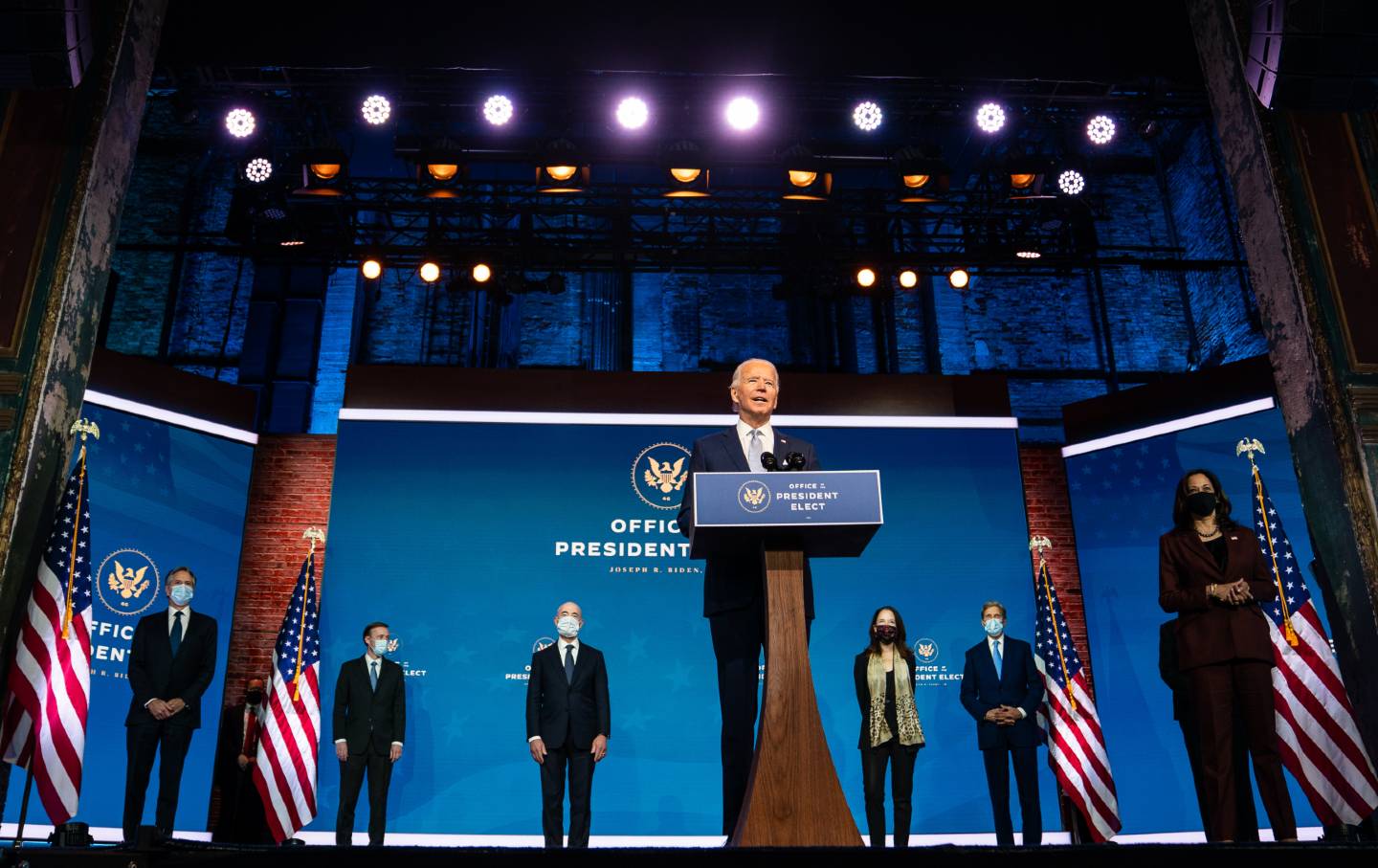 Joe Biden stands on stage with Kamala Harris, Anthony Blinken, Jake Sullivan, Alejandro Mayorkas, Avril Haines, John Kerry, and Linda Thomas-Greenfield