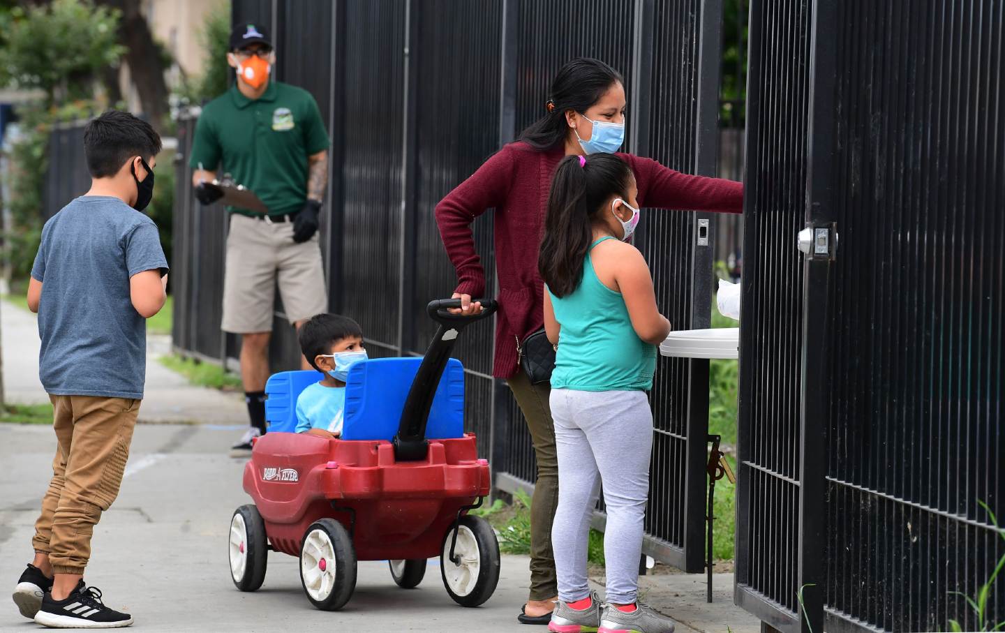 A woman with her children wearing masks, reaches out to pick up a bag of groceries.