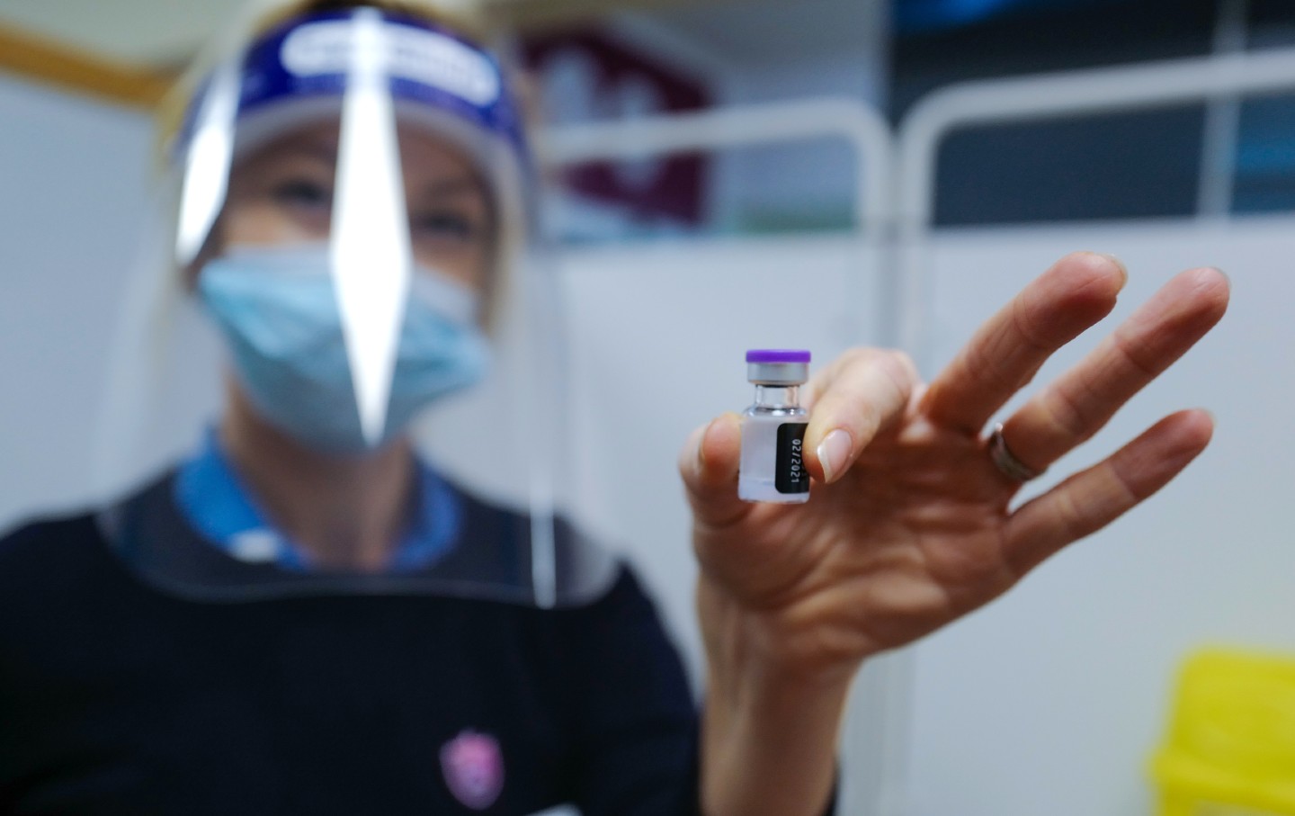 A nurse wearing a surgical mask and face shield holds a vial of the Covid-19 vaccine