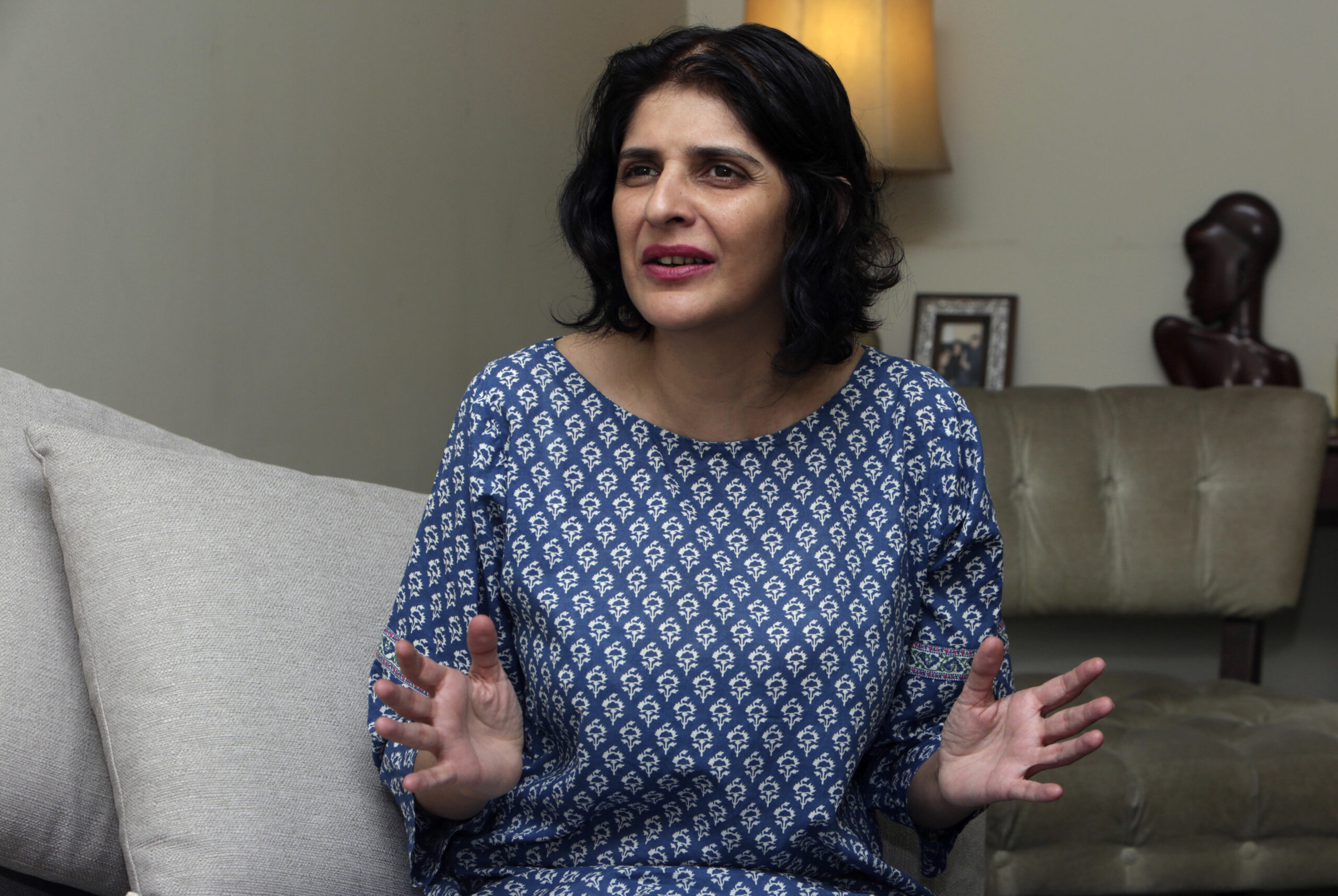 Social media activist, Gul Bukhari, wearing a blue and white printed shirt and pink lip stick, while speaking. She is sitting on a gray couch.