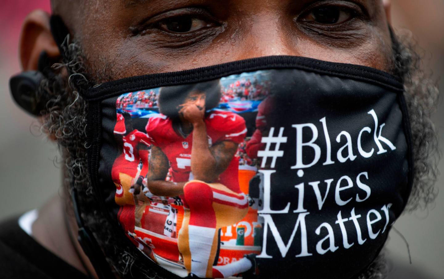 A Black man wearing a mask with Colin Kaepernick kneeling and the words #BlackLivesMatter