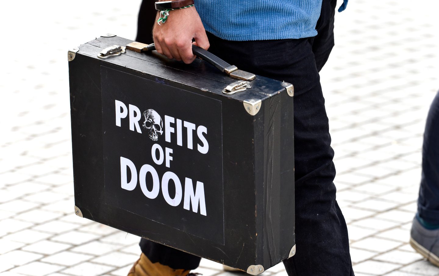 A man carries a briefcase with the words 'Profits of Doom'...