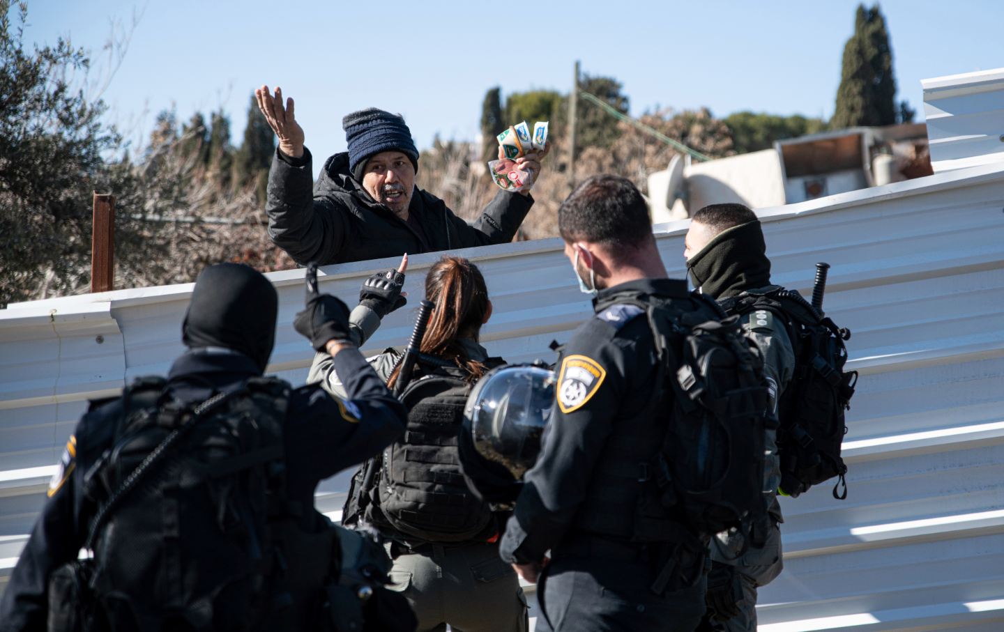 Four Israeli police officers surround a Palestinian man behind a fence.